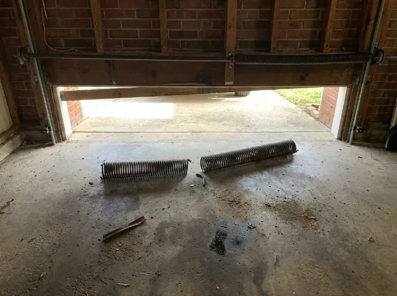 Torsieveer van een sectionale garagepoort boven de opening, gebroken veer ernaast op de vloer
