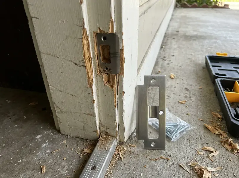 Houten deurkozijn met een uitgebroken sluitplaat na een inbraak, nieuwe versterkte sluitplaat ernaast klaar voor montage