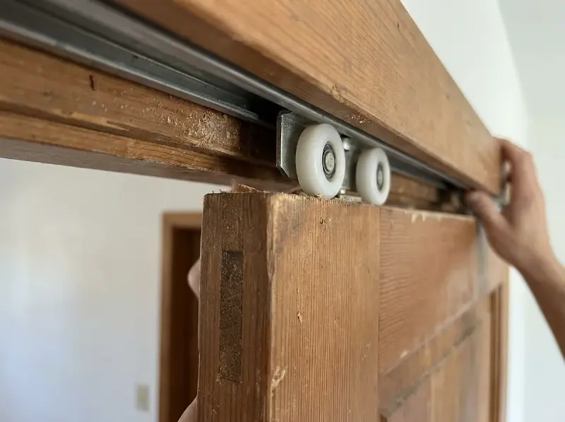 Bovenrail van een houten schuifdeur met nieuwe loopwielen, deur half uitgehangen